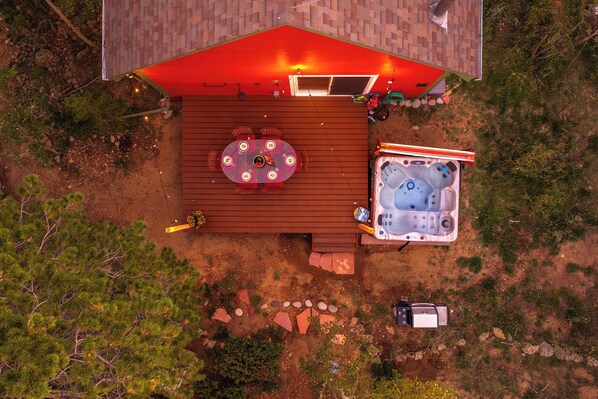 A hot tub and a table with chairs on a wooden deck, surrounded by rocks and trees.