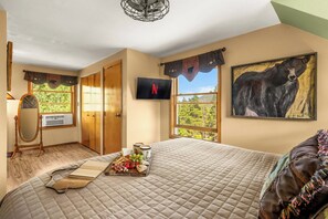 A hotel room with a bed, a television, a painting, and a window with a view of trees. - Arapaho Forest Lodge | Hot Tub, Game Room, Dogs (Black Hawk)