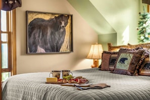 A bed with a quilted blanket, a tray of snacks, and a painting of a bear on the wall.