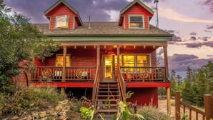 A two-story cabin with a porch, a staircase, and a view of the surrounding landscape.
