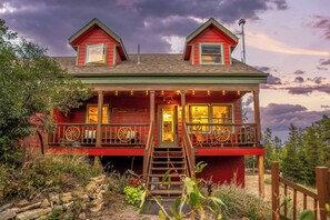 A two-story cabin with a porch, a staircase, and a view of the surrounding landscape.
