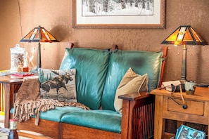 A cozy room with a teal sofa, two lamps, a framed picture on the wall, and a small table with various items.