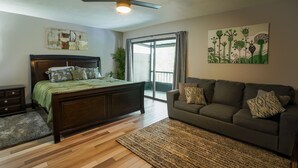 Un dormitorio con cama, sofá, ventilador de techo y un ventanal grande.