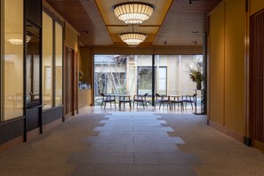 A hallway with a tiled floor, wooden paneling, and a row of chairs facing a large window. - yado-shiontei (Yonago)