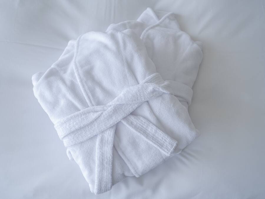 A neatly folded white bathrobe on a white bed.