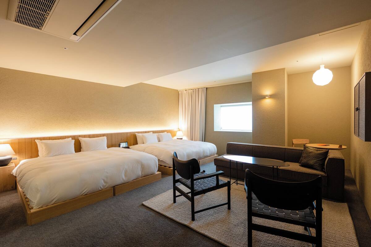 A hotel room with two beds, a sofa, a small table, and a chair.
