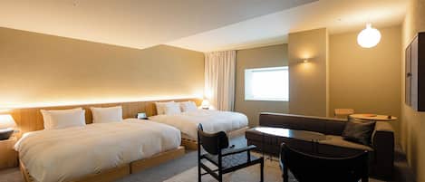 A hotel room with two beds, a sofa, a small table, and a chair.