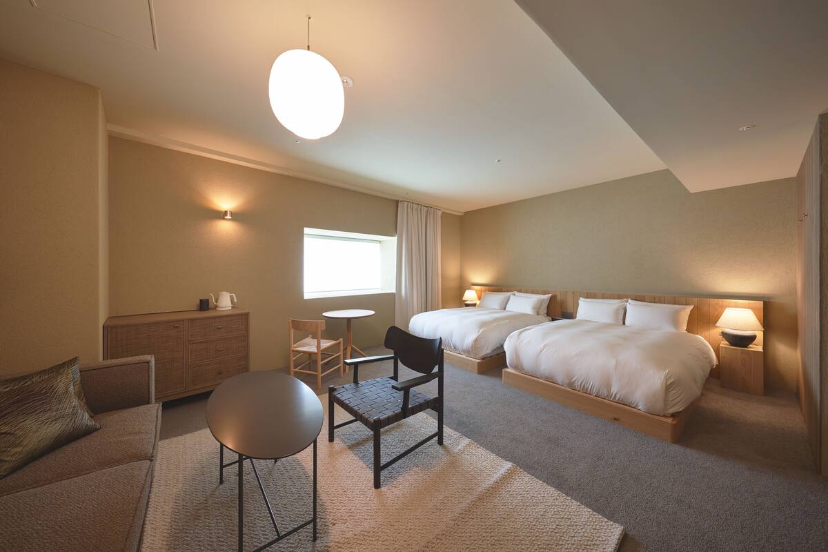 A hotel room with two beds, a sofa, a small table, a chair, a desk, and a lamp.