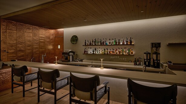 A bar area with wooden flooring, bar stools, a long counter, and shelves with bottles. - HOTEL LEPO CHAHAL (Matsuyama)