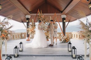 Une cérémonie de mariage mettant en scène un couple sous une pergola en bois, entouré de compositions florales et de lanternes.