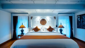 Ein großes Bett mit weißen Leinen und zwei braunen Kissen, an beiden Seiten zwei Nachttische mit Lampen, in einem Zimmer mit dekorativer Decke und einer großen, runden Wandverziierung.