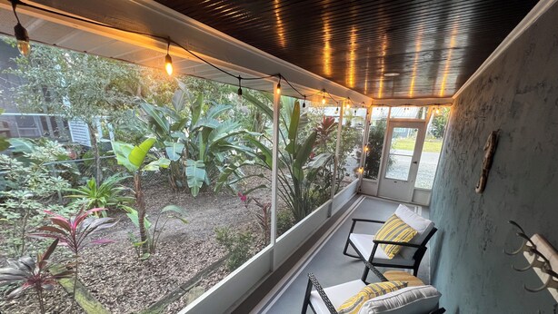Ein Zimmer mit Blick auf einen Garten, ein Fenster mit Lichterkette und ein Sessel mit Kissen.