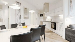 A modern kitchen with white cabinets, a built-in oven, and a dining area with a white table and chairs. - Stunning Apartment in Lübeck Travemünde With 3 Bedrooms, Sauna and Wifi (Lübeck)