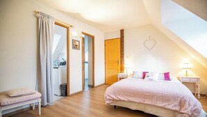 Um quarto com uma cama, mesinhas de cabeceira, um banco, uma porta e uma decoração em formato de coração na parede.