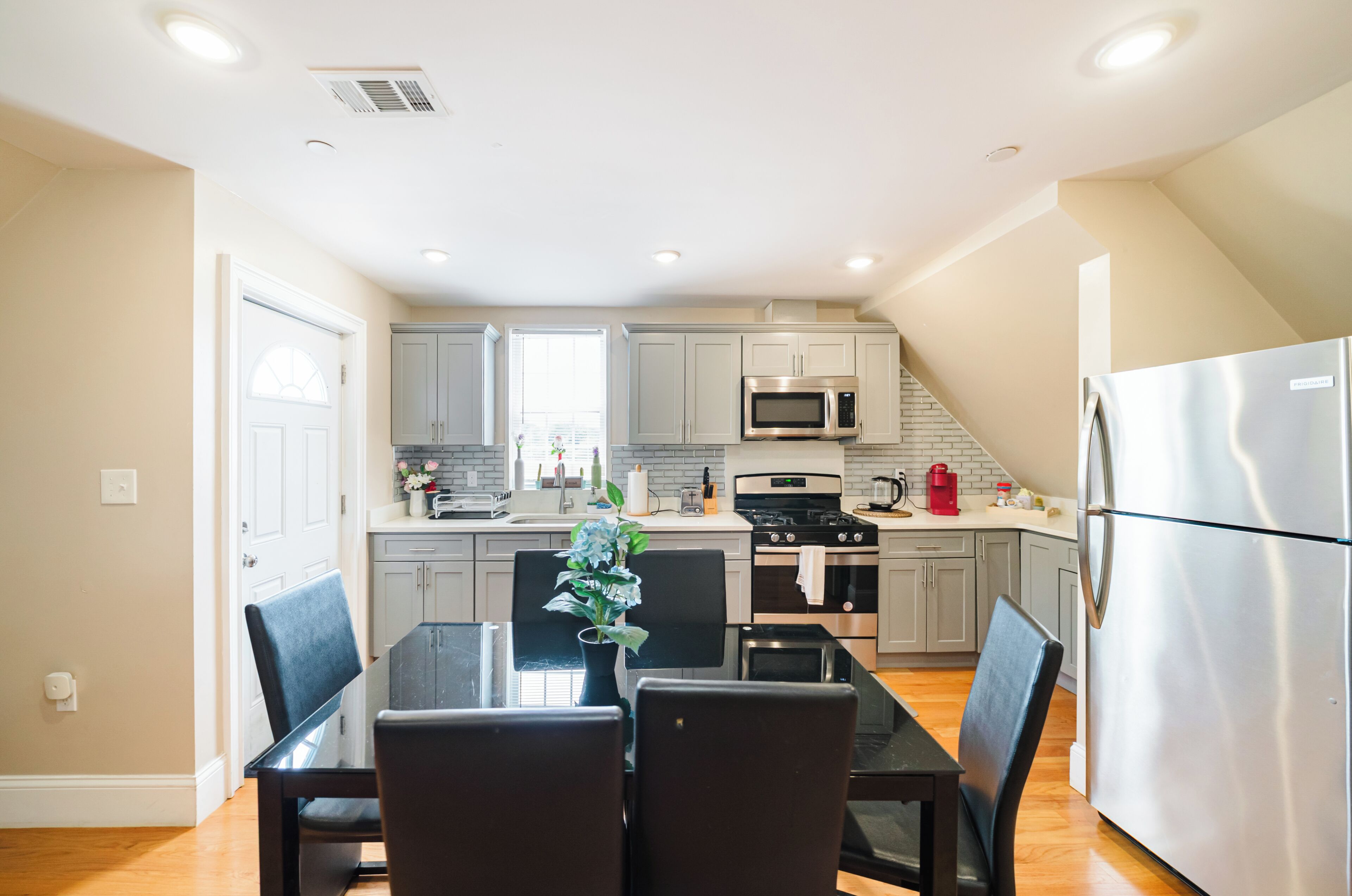 A modern kitchen with grey cabinets, stainless steel appliances, and a dining area with a table and chairs.