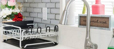 Una cocina con un lavamanos de acero inoxidable, un escurreplatos, una planta en maceta y un letrero que dice 'HOw sweet HOME'.