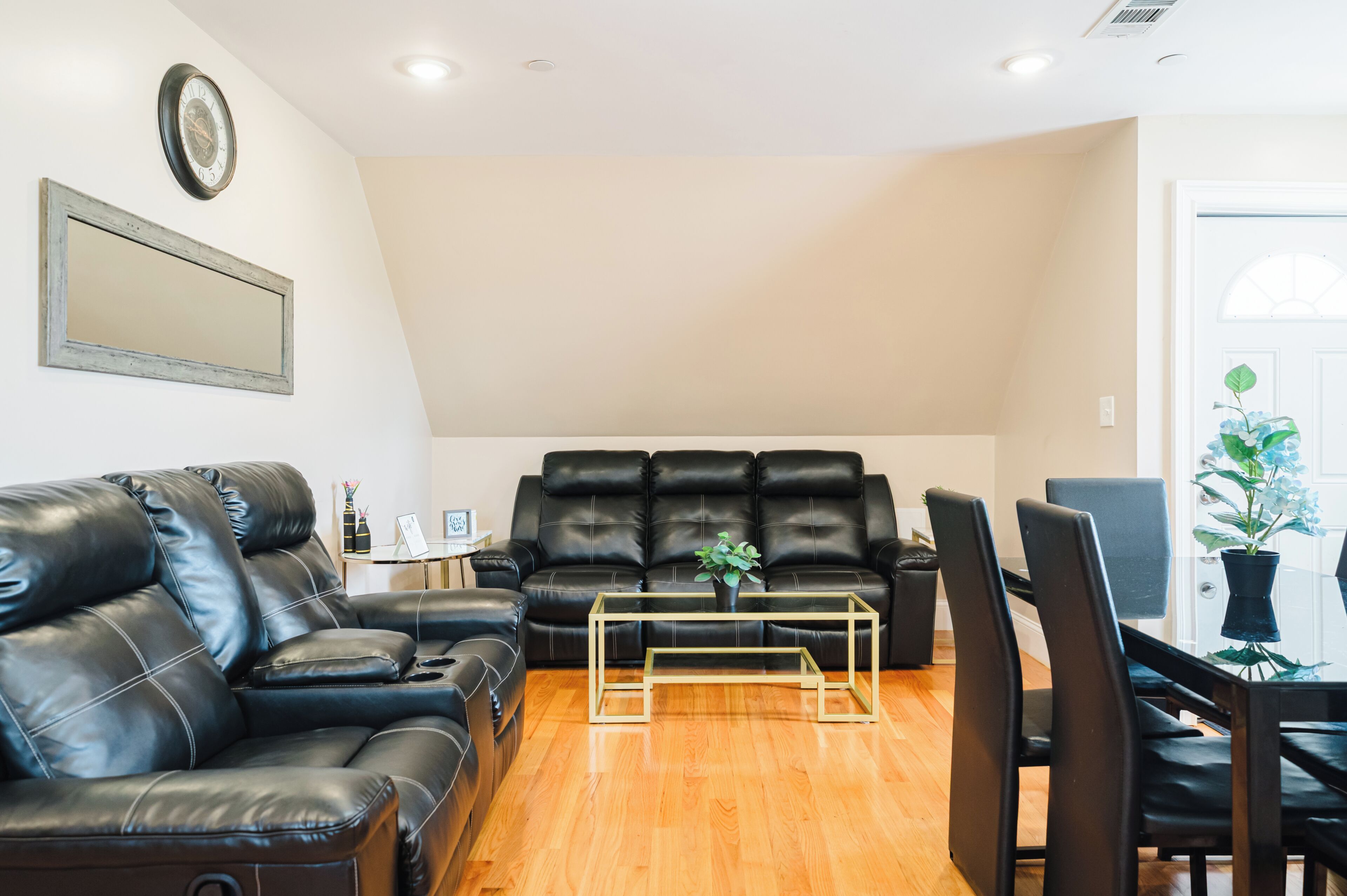 A living room with a black leather sofa, a glass coffee table, and a dining area with chairs.