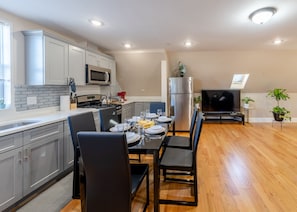 A modern kitchen with grey cabinets, a stainless steel refrigerator, and a dining area with a black table and chairs.