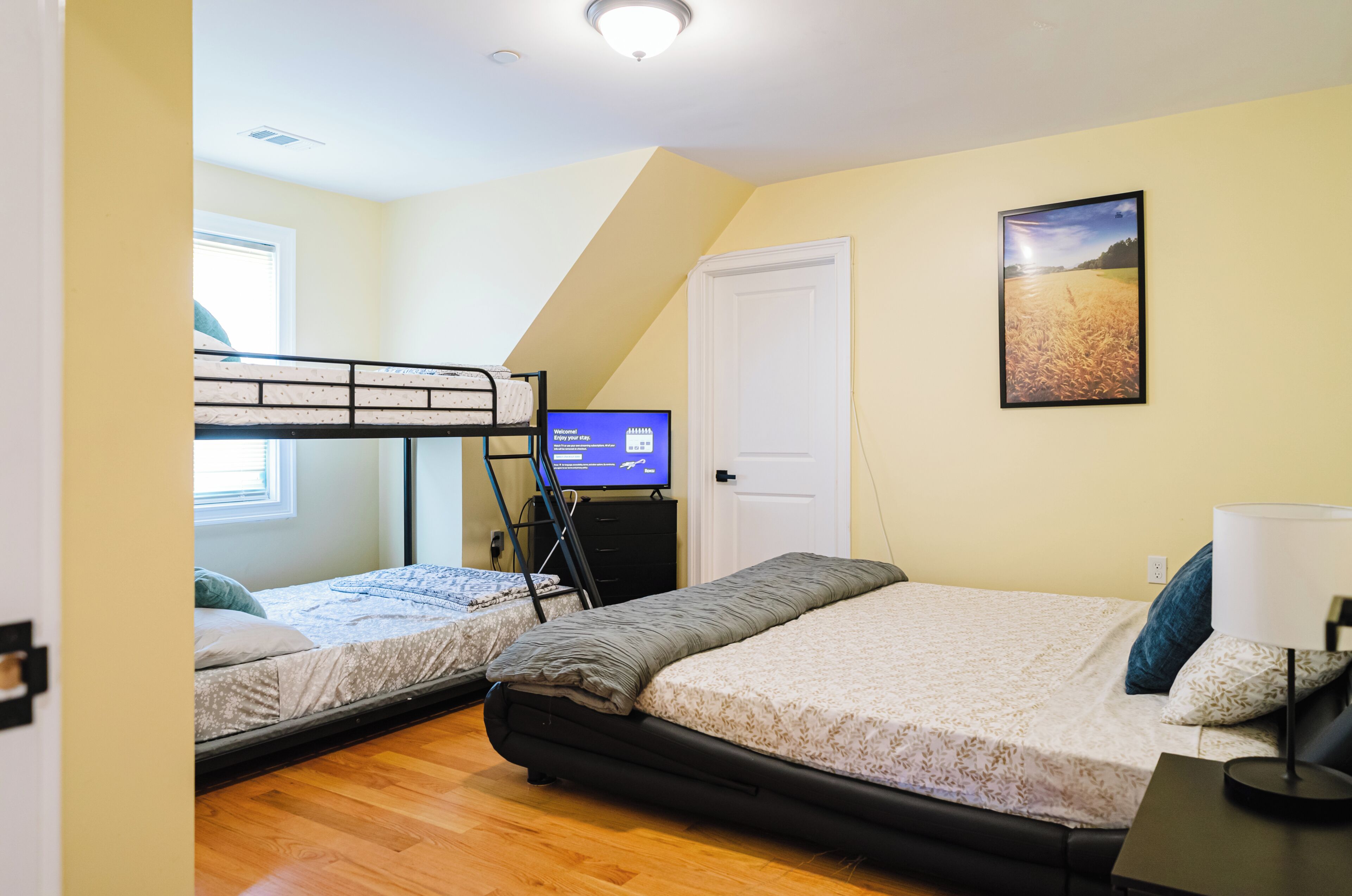 A bedroom with two beds, a television, a door, and a window.