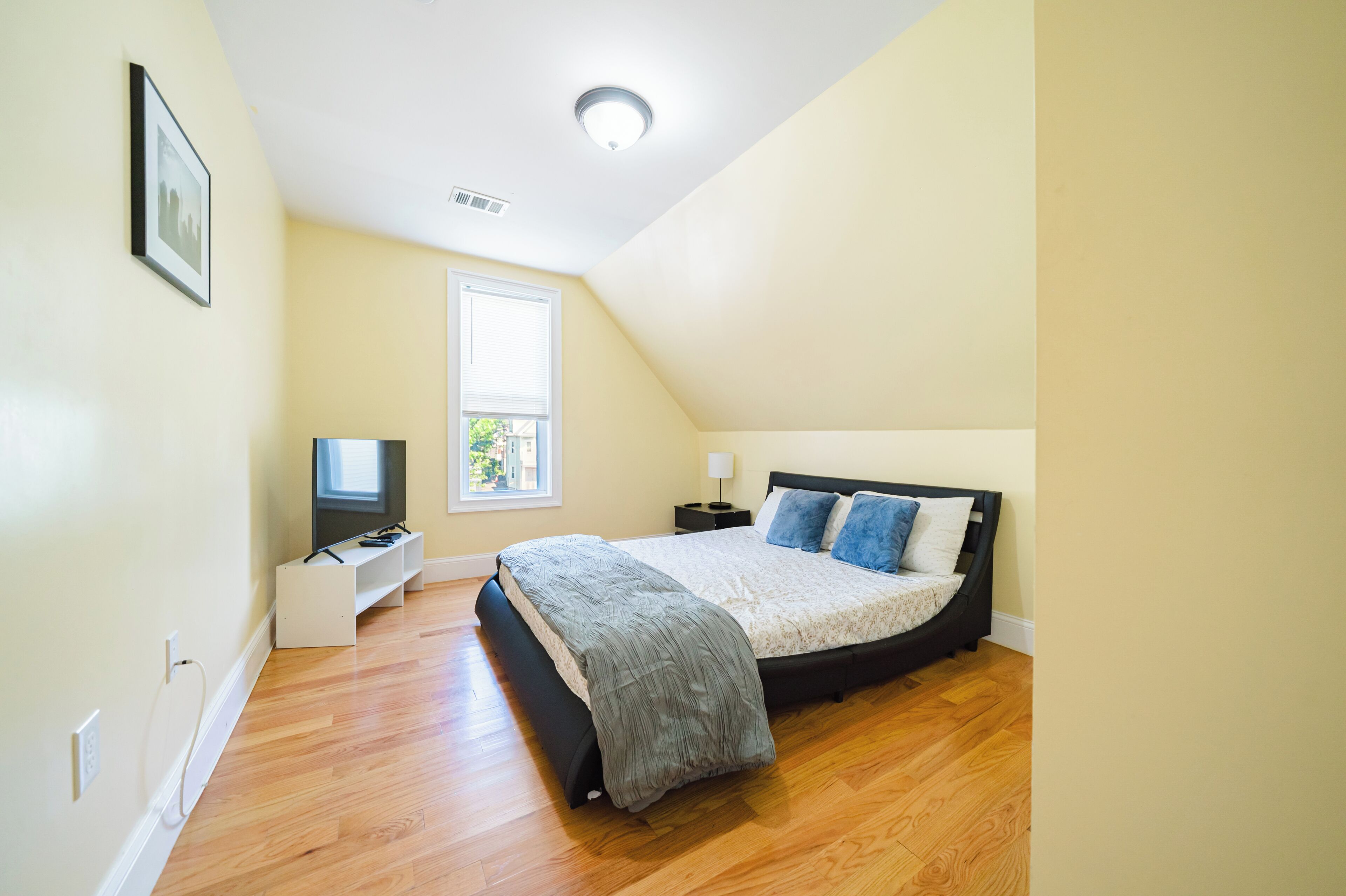 A bedroom with a bed, a TV, a bedside table, and a window.