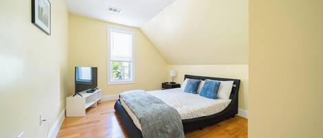 A bedroom with a bed, a TV, a bedside table, and a window.