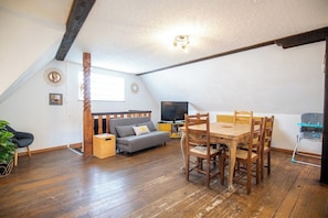 Ein Loft-Zimmer mit Esstisch, Stühlen, einer Couch, einem Fernseher und einem Holzbalken an der Decke.