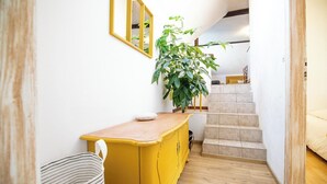 A hallway with a yellow cabinet, a striped bag, a plant, and a staircase leading to a room. - Gîtes Rocher des Celtes (Dieffenthal)