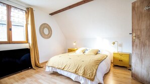 A bedroom with a bed, wooden floor, a round wall decoration, a wardrobe, and a window with curtains. - Gîtes Rocher des Celtes (Dieffenthal)