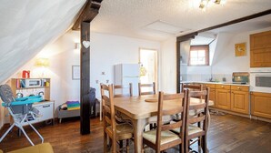 A cozy kitchen with wooden furniture, a dining table, and a high ceiling with exposed beams. - Gîtes Rocher des Celtes (Dieffenthal)