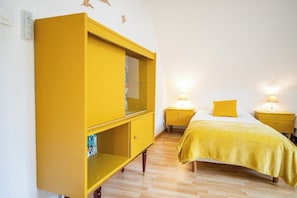 Ein Zimmer mit einem Bett, zwei Nachttischen mit Lampen, einem gelben Kleiderschrank und einem an der Wand befestigten Lichtschalter.