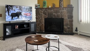 A living room with a stone fireplace, a television displaying a moose, and a small round table with coasters.