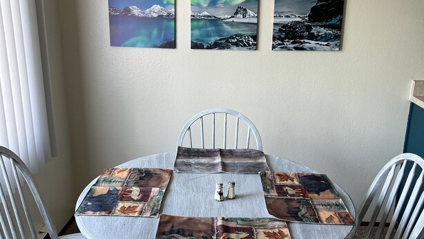 A dining table with a rustic design, surrounded by four chairs, set against a wall with three framed photographs depicting natural landscapes.