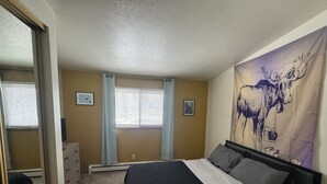 A bedroom with a bed, a dresser, a window with blinds, and a wall tapestry.