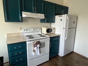 A compact kitchen with teal cabinets, a white stove, a microwave, and a refrigerator. - One bedroom top floor condo with Mountain View from bedroom and covered parking (Anchorage)