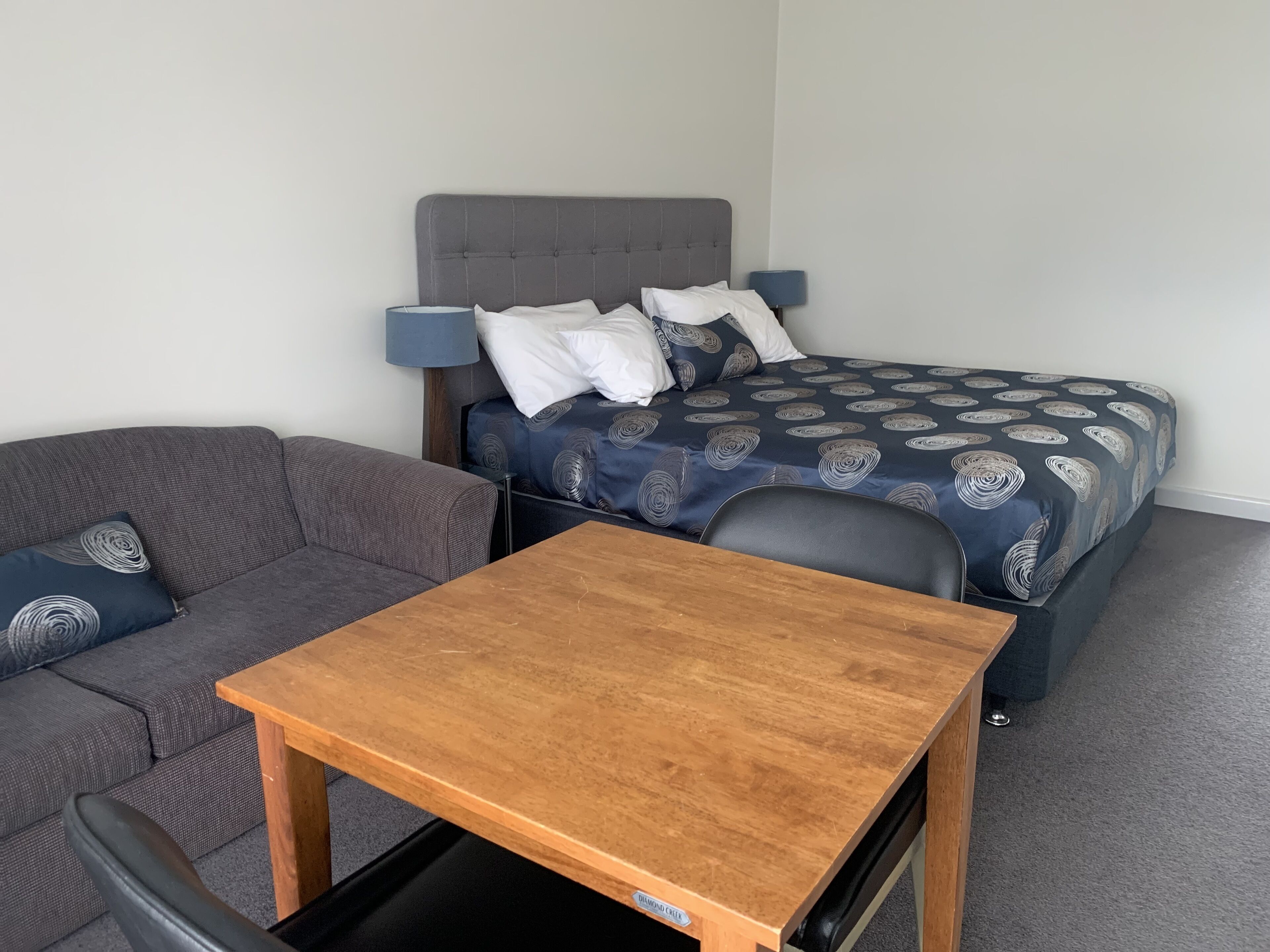 Ein Schlafzimmer mit einem Bett, einem grauen Sofa, einem Holztisch und einem Stuhl.