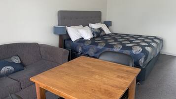 Ein Schlafzimmer mit einem Bett, einem grauen Sofa, einem Holztisch und einem Stuhl.