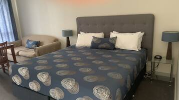 A neatly arranged bedroom with a large bed, two bedside tables, a chair, and a lamp.