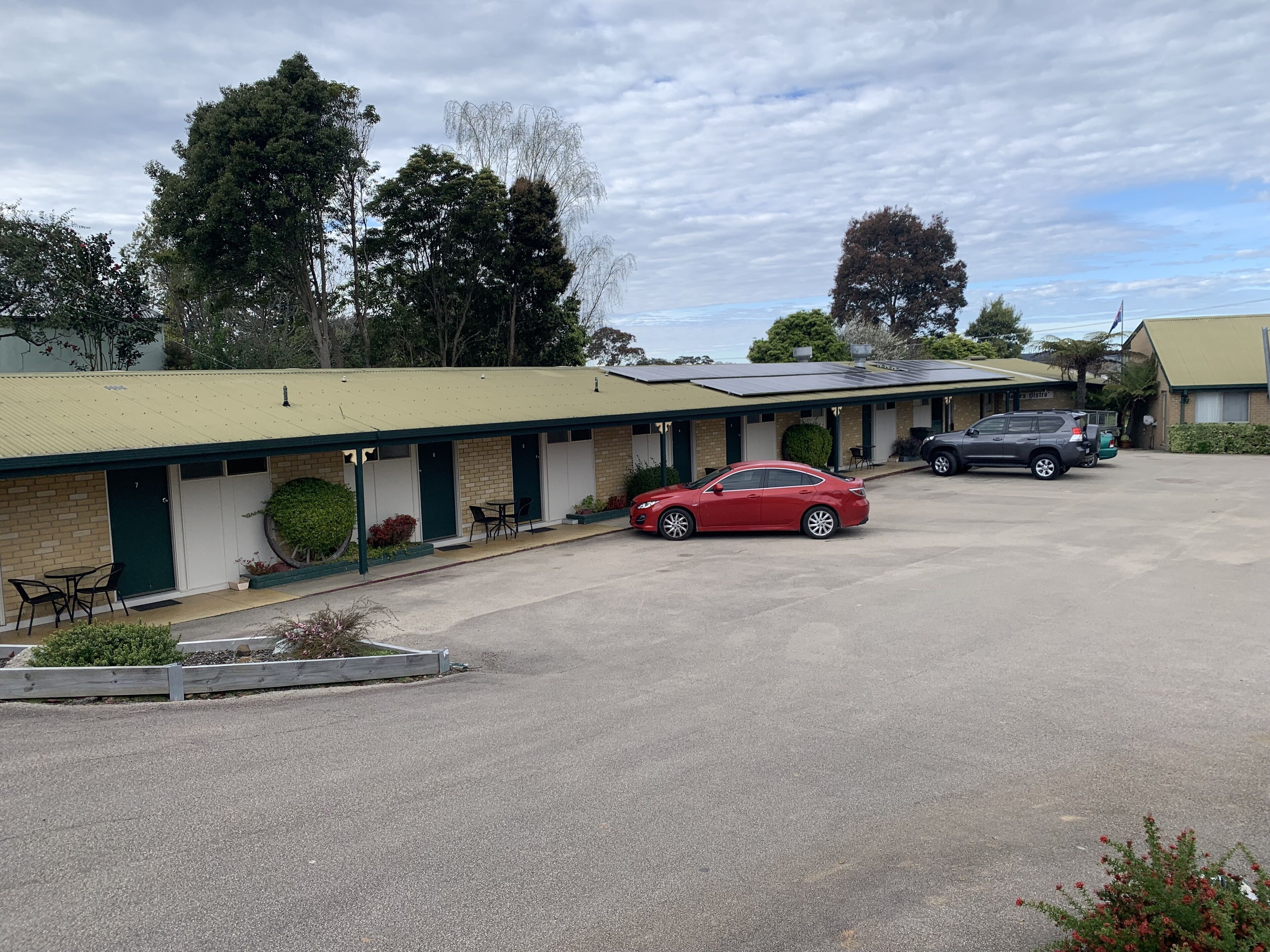 Un motel con varias habitaciones, una zona de estacionamiento techada y un pequeño jardín.