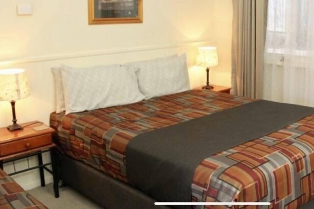 A hotel room with a bed, two bedside tables, a lamp, and a window with curtains.