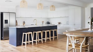 A modern kitchen with white cabinets, a central island with stools, and hanging wicker light fixtures. - Deja Blue Anna Bay (Anna Bay)