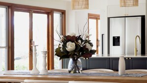 A dining table with a vase of flowers, a candle, and a placemat. - Deja Blue Anna Bay (Anna Bay)