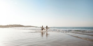 Two people walking on a beach with surfboards, heading towards the ocean. - Deja Blue Anna Bay (Anna Bay)
