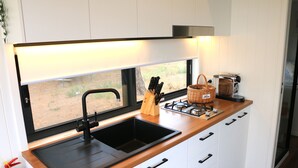 Una cocina compacta con un lavamanos negro, armarios blancos, una ventana con vistas al exterior y una estufa a gas.
