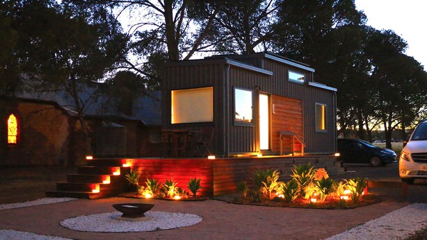 Una casa moderna con fachada de madera, una escalera visible y un camino de entrada con grava y plantas.