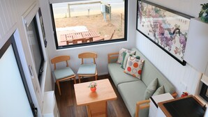 Un espacio habitable compacto con sofá, dos sillas, una mesita, ventana con vistas a un área exterior y una obra de arte colgada en la pared.