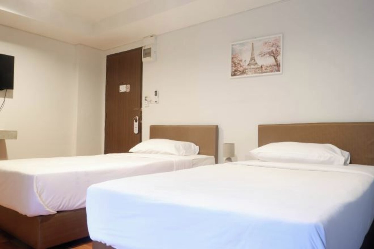 Ett hotellrum med två separata sängar, en trädörr, en väggmonterad TV och en inramad bild av Eiffeltornet.