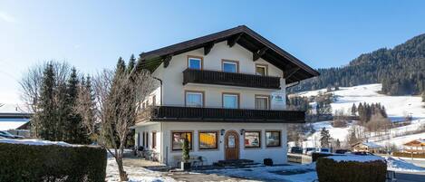 Een gebouw met twee verdiepingen, een balkon en een bord met de tekst 'Villa by you', met een besneeuwd landschap op de achtergrond.