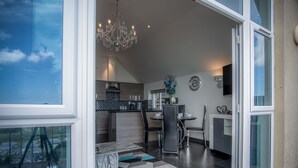 A modern kitchen with a chandelier, a dining area with a table and chairs, and a large window with a view of the sky. - Nautilus - 2 Bedroom Apartment - Pendine (Carmarthen)