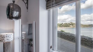 A room with a large window overlooking a coastal area, a floor lamp, and a framed picture on the wall.