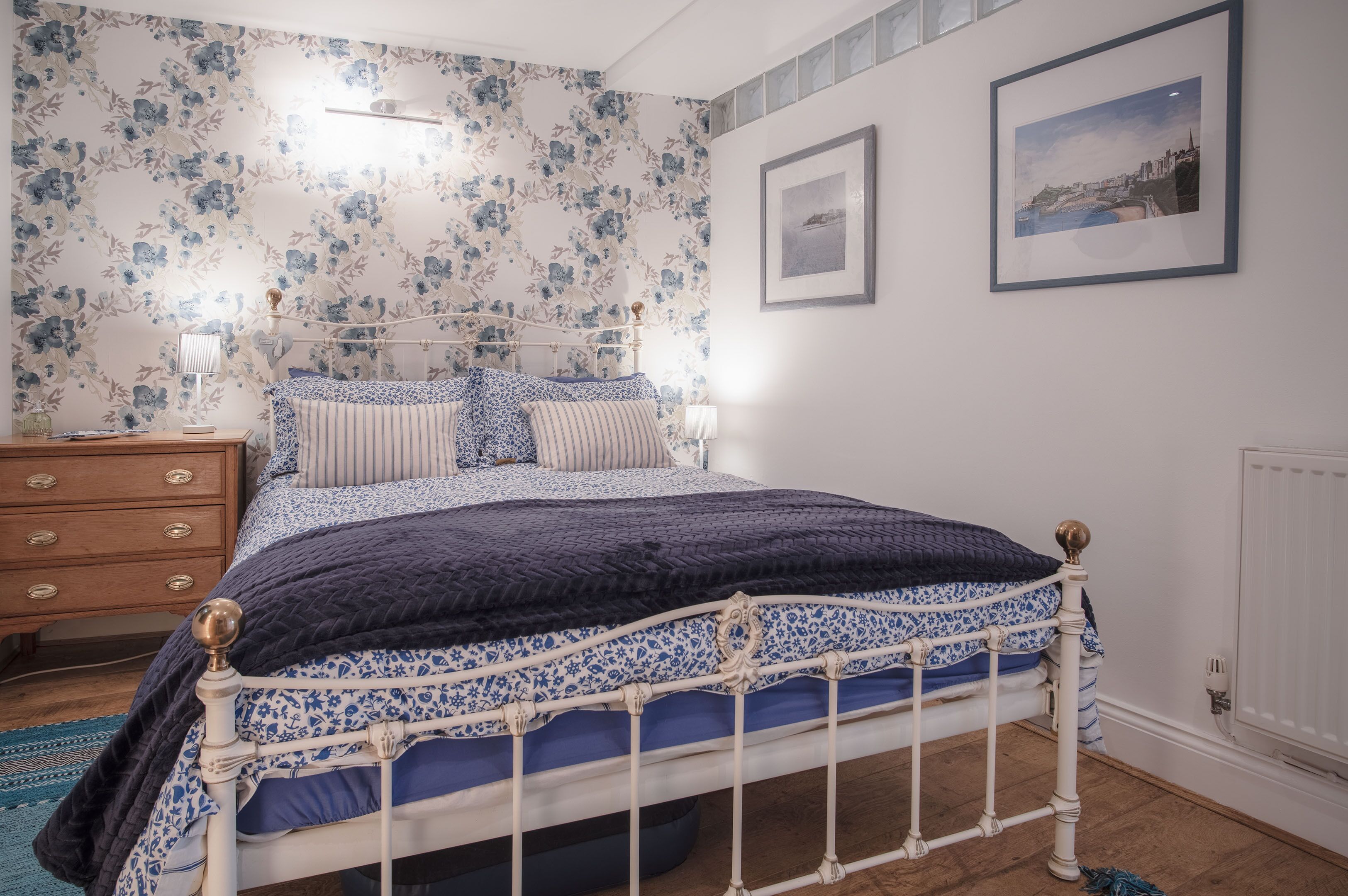 Quarto com cama, cômoda de madeira e papel de parede floral.